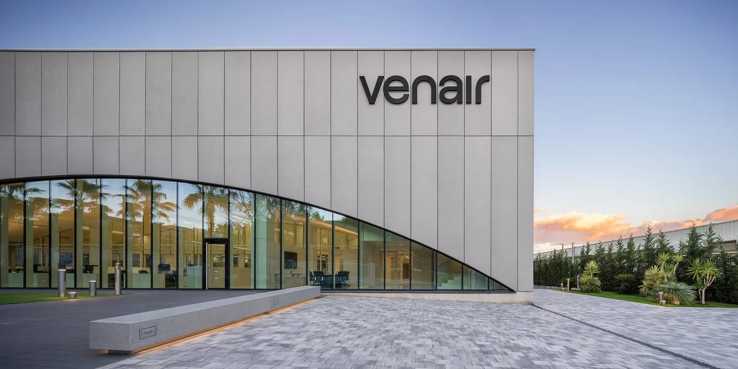 Entrada de la sede de Venair: el logotipo sobre el muro de paneles grises y un gran arco acristalado que deja ver las oficinas, con palmeras al atardecer.